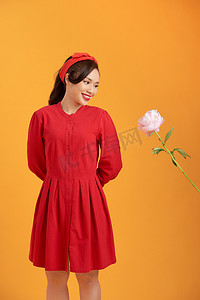 迷人的年轻亚洲人身穿红色连衣裙，手捧牡丹花，在橙色背景中被隔离。
