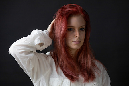 美丽的红发年轻女子的画像，手插在头发中。
