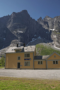 Rauma Railway Station 是一座历史悠久的木制建筑，位于著名的风景秀丽的铁路上，位于 Troll Wall 下方，陡峭的垂直岩面，Rauma Municipality，More Og Romsdal，挪威