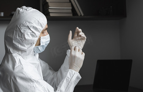 隔离期间，身穿防护服和医用口罩的男子在家中的工作场所戴着橡胶手套。