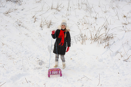 一个带着雪橇的女孩站在多雪的草地上