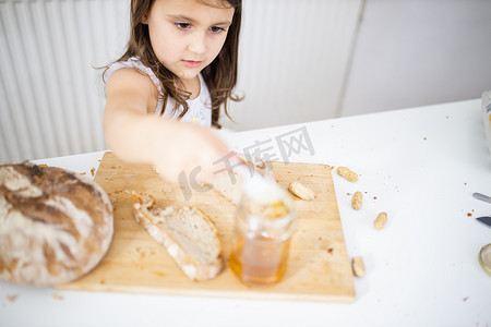 采蜂蜜摄影照片_小女孩从面包片旁的罐子里采蜂蜜