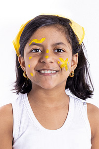 儿童脸上摄影照片_快乐的小女孩，脸上涂着彩绘来庆祝黄色的日子