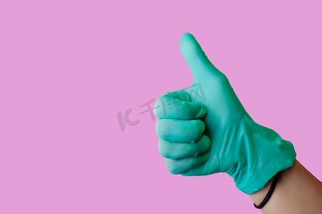 蓝色运营摄影照片_戴着蓝色乳胶手套的女手竖起大拇指，就像浅粉色背景上孤立的手势一样。