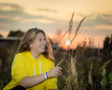 一个年轻的女孩在草地上，在夕阳的照射下长满了高高的草。
