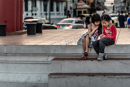 两个女孩坐下来看着大秋千 (Sao Ching Cha) 的手机照片。