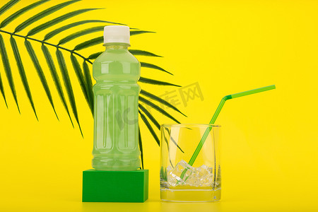 绿色底座上的绿色热带夏季鸡尾酒，玻璃杯里装满冰块，黄色背景上的绿色稻草