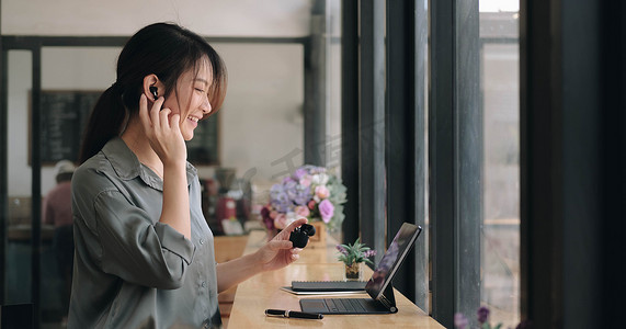 亚洲年轻女孩的特写使用无线耳塞在咖啡馆通过笔记本电脑进行在线语言课程和搜索信息。
