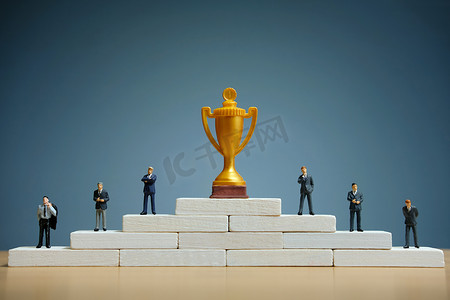 领奖摄影照片_商业战略概念照片 — 商人的缩影站在领奖台上，拿着金奖杯