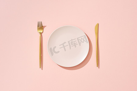 粉红色背景中的刀、淡粉色盘子和叉子