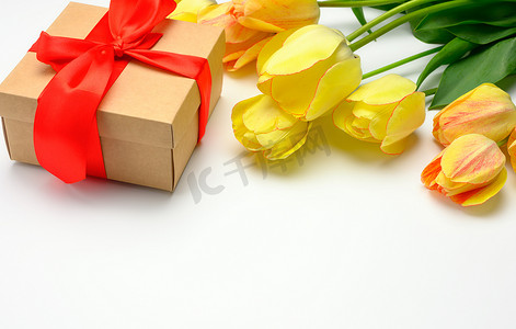 方形盒子白色摄影照片_黄色郁金香和方形盒子，白色背景上系着红丝带，母亲节的节日背景