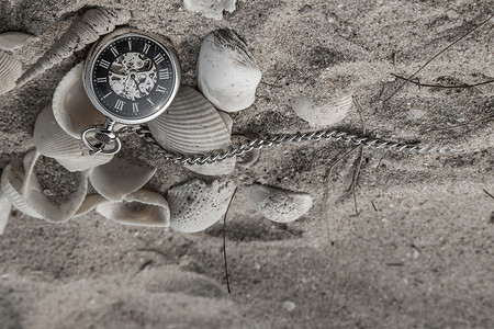 沙滩上沙子中的古董怀表和贝壳。