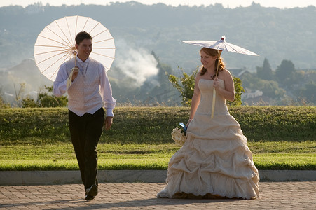 新娘和新郎在阳光下散步，雨伞跳跃