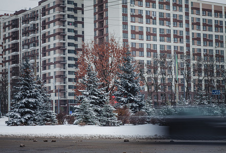 一辆行驶中的汽车在雪中的冬季道路上沿着一座高楼行驶