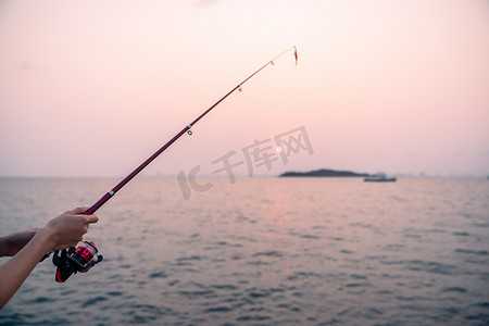 女人手拿着海面背景的钓鱼竿，在日落时钓鱼。