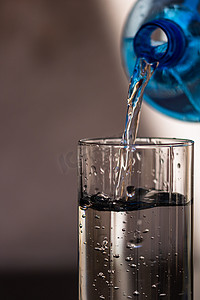 在模糊的背景下将蓝色塑料瓶中的水倒入玻璃杯中。