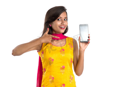 年轻漂亮的女人拿着并在白色背景上展示空白屏幕智能手机或手机或平板电脑。
