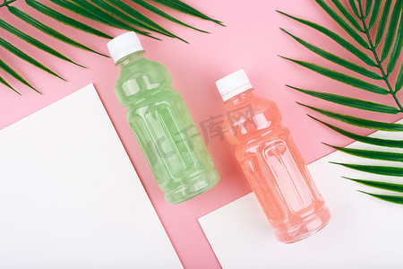 创意公寓铺有两瓶粉色和绿色排毒饮料，粉色和白色背景上带有棕榈叶