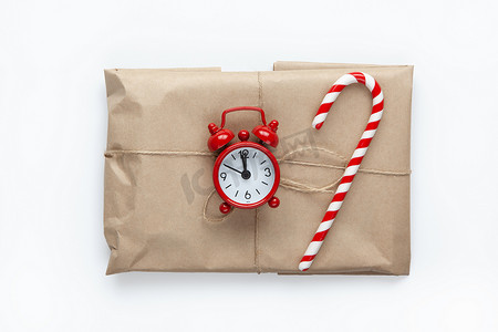 用棕色牛皮纸包裹的圣诞礼物，系着鞭子，装饰着白色背景的甘蔗糖和小模拟钟。