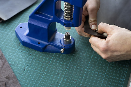 工匠使用手压机在皮革上设置按扣以制作钱包。