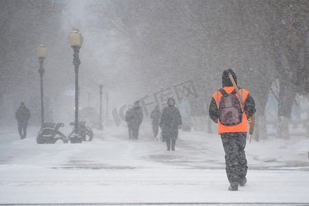极端的摄影照片_市政服务的一名工作人员带着雪铲在暴风雨、暴风雪或冬季降雪中在城市的恶劣天气中沿着道路行走。北方的极端冬季天气条件。