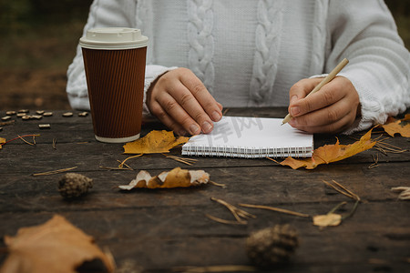 注意事项ppt素材摄影照片_人手端着一杯咖啡，围巾放在木桌上，桌上放着笔记本、钢笔和秋叶。