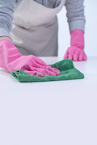 粉色弥散摄影照片_围裙的年轻女管家戴着粉色手套清洁桌子，预防病毒感染的概念，家政服务，特写。