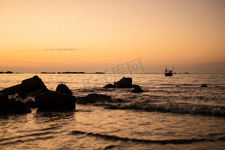 金色图图摄影照片_缅甸 Ngwesaung 附近的海滩上，金色的夕阳映照着岩石和海浪中的一艘船