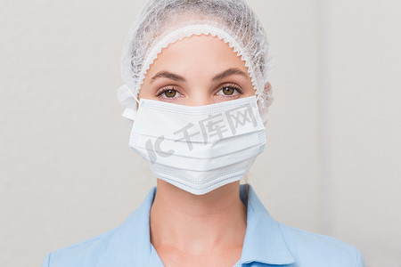 护士戴口罩摄影照片_戴着外科口罩和帽子的牙医看着相机