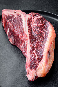 肉丁摄影照片_黑木桌背景上，盘子上的干熟生丁骨或牛排牛肉大理石纹肉牛排