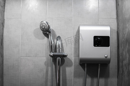即热式无水箱电热水器安装在灰色瓷砖墙上，带有输入和输出管出口和 elcb 安全断路器系统和银色淋浴。