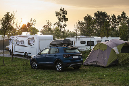 大篷车车摄影照片_露营地绿色草地上的大篷车和露营者。