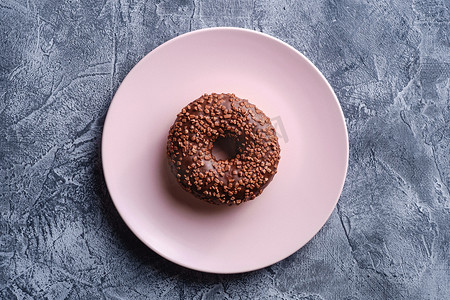 粉色盘子上洒着巧克力甜甜圈，混凝土质感背景上的甜釉甜点食品，顶视图