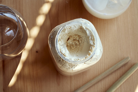 塑料罐中的乳清蛋白粉，背景是乳清蛋白饮料和竹吸管