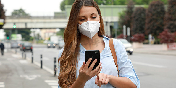 COVID-19 年轻女性佩戴 KN95 FFP2 口罩在城市街道使用智能手机应用软件帮助接触者追踪和自我诊断以应对 2019 年冠状病毒大流行