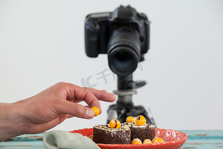 摄影师把黄樱桃放在甜点上，背景是相机
