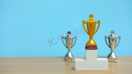 站在白色领奖台上的金色奖杯，后面有两个银色奖杯