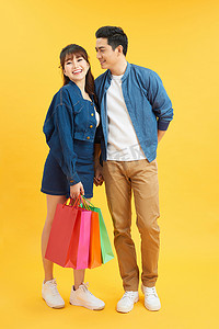 快乐的年轻夫妇带着购物袋拥抱，看着对方孤立在黄色