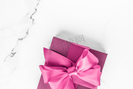 大理石背景上带丝绸蝴蝶结的粉红色礼盒、女婴淋浴礼物和奢华美容品牌的魅力时尚礼物、假日平板艺术设计