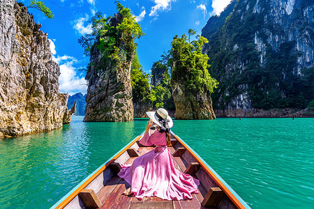女孩望天空摄影照片_美丽的女孩站在船上，望着泰国素叻他尼省考索国家公园 Ratchaprapha 大坝的群山。