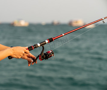 女人手拿着海面背景的钓鱼竿，在日落时钓鱼。