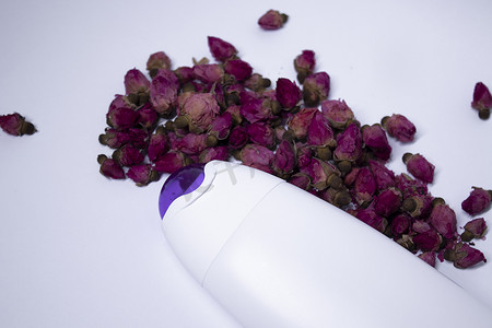 白色洗发水瓶，颈部为紫色，没有标签，靠近一堆小粉红玫瑰。