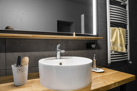 木台摄影照片_浴室内部墙壁上铺有灰色瓷砖，时尚的圆形水槽和橡木台面上的水龙头。
