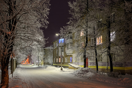 夜晚的街道上，在灯笼和房屋的窗户下，白雪皑皑的树木被涂成不同的颜色。