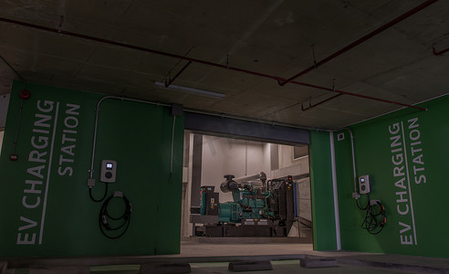 发电机房应急电源的前视图，房外墙上有服务电动汽车充电站和电池。