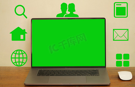 一个抽象的绿色屏幕笔记本电脑和鼠标放置在一张长桌上，图标显示符号以利用各种程序。