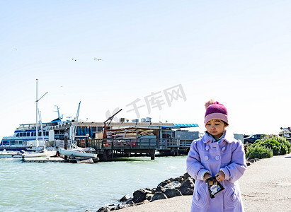 穿着紫色外套和可爱帽子的漂亮女孩在加利福尼亚州索萨利托的海湾地区散步和吃零食