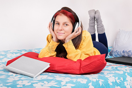 躺在床上的女孩带着耳机、书和笔记本电脑