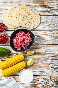 轻卡摄影照片_用切碎的有机肉、玉米、卡尔萨在白色纹理木桌上烹制墨西哥炸玉米饼配料，顶视图有文字空间。