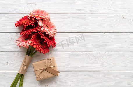 红色非洲菊雏菊花和工艺礼盒，白色木桌上有标签